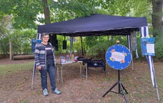Der Stand von Sprachbrücke-Hamburg e.V. bei der „Lokstedt-Rallye 2024“. Im Hintergrund Bäume, vor dem Stand das Glücksrad von Sprachbrücke-Hamburg e.V.