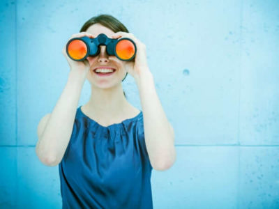 Junge Frau mit Fernglas schaut in die Kamera