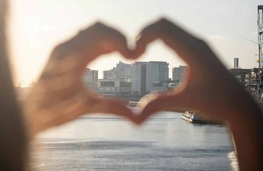 Herzförmige Hand mit Blick auf die Skyline von Hamburg
